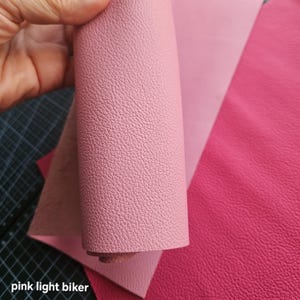 Könnte beinhalten: Nahaufnahme von rosa Lederplatten in verschiedenen Farbtönen. Das obere Blatt ist hellrosa, gerollt, um eine strukturierte Oberfläche freizulegen. Weitere Blätter sind hellrosa und ein tieferes Magenta. Der Text "pink light biker" ist sichtbar.