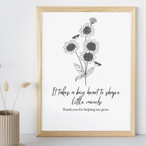 Puede incluir: Una impresión enmarcada con un marco de madera clara. La impresión presenta una ilustración floral en blanco y negro de girasoles y mariposas. El texto dice: "Se necesita un gran corazón para dar forma a las mentes pequeñas. Gracias por ayudarme a crecer."