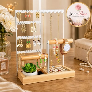 May include: A white metal and light wood jewelry display stand featuring multiple hooks for necklaces, perforated bars for earrings, a horizontal bar for bracelets and watches, and a rectangular base tray with a small potted succulent.