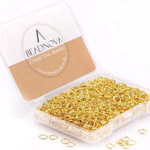 May include: A clear plastic container filled with gold-colored jump rings. The container is open, revealing a large quantity of the rings. The lid has the text "BEADNOVA Create Your Jewelry" printed on it.