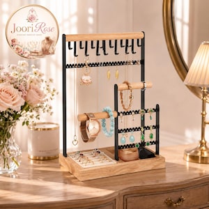 May include: A tiered jewelry organizer stand featuring a light wood base and horizontal bars, combined with black metal frames. The stand includes hooks for necklaces, perforated bars for earrings, and a small tray for rings, holding various jewelry items.