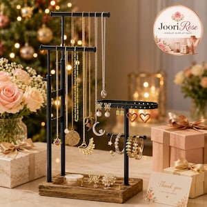 May include: A black metal jewelry display stand with a wooden base, featuring multiple tiers for hanging necklaces and earrings. The stand holds various gold-toned necklaces with pendants, including a moon and wing design, and several pairs of earrings.