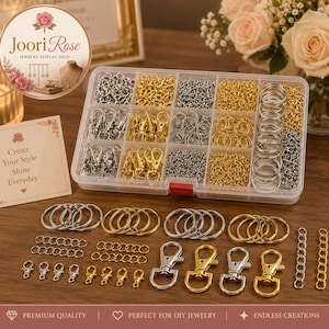 May include: A clear plastic storage container filled with assorted metal jewelry findings including silver and gold-toned lobster claw clasps, jump rings, and split key rings. Additional loose metal components are arranged on the surface.