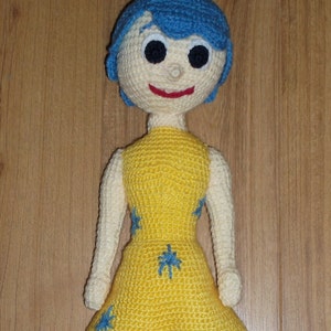 Può includere: Una bambola all'uncinetto con capelli blu, un vestito giallo con disegni di stelle blu e un viso sorridente.