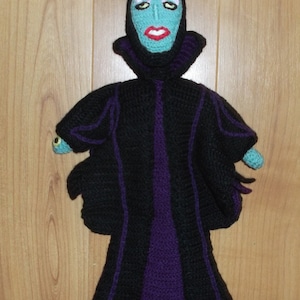 Puede incluir: Una muñeca de Maléfica hecha a crochet de la película de Disney La Bella Durmiente. La muñeca lleva una túnica negra y morada con un sombrero puntiagudo y tiene una cara verde con labios morados.