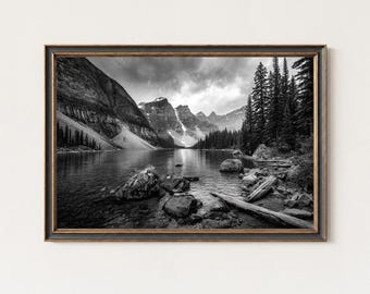 May include: Black and white framed print of a serene mountain lake scene. The image features a calm lake reflecting the surrounding mountains and trees. The frame is dark with a distressed finish, adding a vintage aesthetic to the landscape photograph.