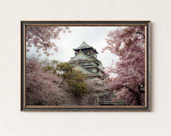 Pode incluir: Impressão emoldurada do Castelo de Osaka no Japão, rodeada por cerejeiras em flor. O castelo apresenta uma estrutura de vários níveis com um telhado verde e detalhes dourados. A imagem é emoldurada em uma borda escura e ornamentada.