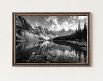 May include: Black and white framed print of a mountain lake scene. The image features a serene lake reflecting the surrounding mountains and sky. The frame is a dark color with a gold trim.