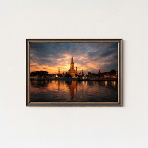 Peut inclure: Impression encadrée d'un temple au coucher du soleil. L'image présente un temple doré avec une haute flèche centrale et plusieurs flèches plus petites, reflétées dans l'eau en contrebas. Le ciel est un mélange d'orange, de jaune et de bleu.