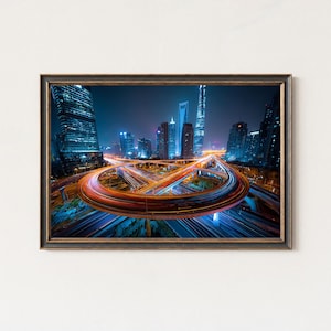 May include: Framed print of a nighttime cityscape featuring illuminated skyscrapers and a complex highway interchange. The image showcases long exposure light trails from vehicles, creating streaks of red and orange against a backdrop of blue-lit buildings.