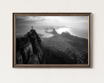 May include: Black and white framed print of Christ the Redeemer statue atop Corcovado Mountain overlooking Rio de Janeiro, Brazil. The image captures the city, Guanabara Bay, and Sugarloaf Mountain under a cloudy sky.