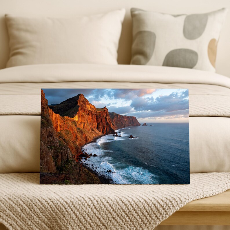 K&ouml;nnte beinhalten: Leinwanddruck einer K&uuml;stenlandschaft mit einer dramatischen Klippe, die von der untergehenden Sonne beleuchtet wird. Das Bild zeigt eine zerkl&uuml;ftete K&uuml;stenlinie mit Wellen, die gegen die Felsen schlagen, und einen weiten Ozean unter einem bew&ouml;lkten Himmel. Die Farbpalette umfasst warme Orange-, Braun- und Blaut&ouml;ne.