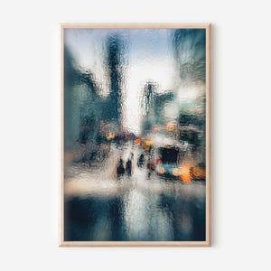 May include: Abstract art print of a city street scene, framed in light wood. The image is blurred, with a focus on the textures of the glass and the lights of the city. The colour palette includes blues, greens, and oranges.
