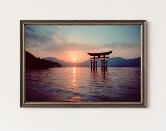 May include: Framed print of a Japanese torii gate at sunset. The gate stands in the water, with the sun setting behind it, casting a golden glow on the water. The sky is a mix of orange, pink, and blue.