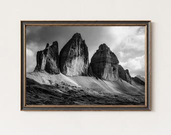May include: Monochrome framed print of the Tre Cime di Lavaredo mountains in the Italian Dolomites. The image shows the dramatic peaks under a cloudy sky, presented in a dark, rustic frame.
