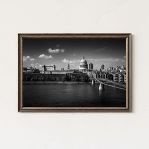 Puede incluir: Impresión enmarcada en blanco y negro del horizonte de Londres, con la Catedral de San Pablo y un puente sobre el río Támesis. La imagen tiene una estética vintage, en un marco de madera oscura.
