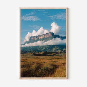 Può includere: Una stampa incorniciata di un paesaggio montano con una montagna dalla cima piatta parzialmente nascosta dalle nuvole. Il cielo è blu con nuvole bianche. Il primo piano mostra un campo di erba secca.