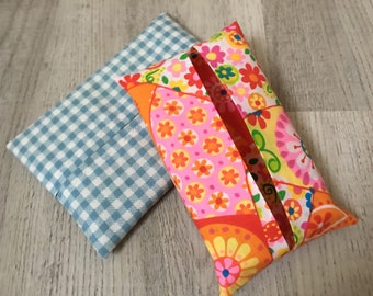 Pode incluir: Duas capas de tecido para caixa de lenços de papel. Uma é azul e branca xadrez, a outra é rosa, laranja e amarela com um padrão floral.