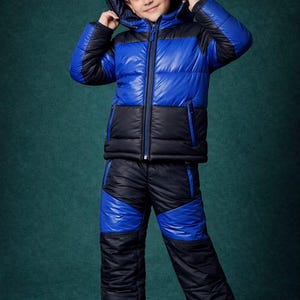 Może przedstawiać: Niebiesko-czarny zestaw kurtki i spodni pikowanych z kapturem. Kurtka i spodnie mają pikowany wzór. Dziecko ma na sobie białe trampki. Strój jest przeznaczony na zimną pogodę.