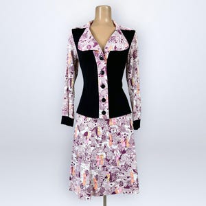 May include: A two-piece outfit consisting of a long-sleeved jacket and a knee-length skirt. The jacket features solid black panels on the front and cuffs, with a white, purple, and orange patterned fabric on the collar, sleeves, and skirt.