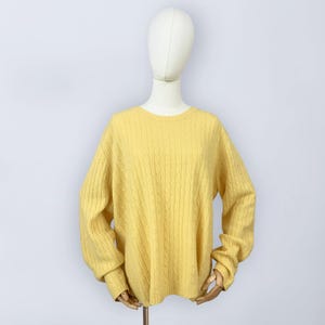 May include: A yellow cable-knit sweater with a crew neck and long sleeves. The sweater is displayed on a mannequin against a white background. The knit pattern is visible across the front and sleeves.