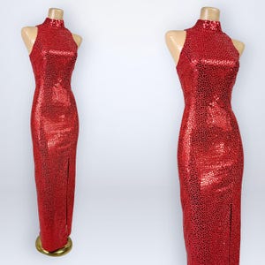 May include: A floor-length red dress featuring a high neckline and a sleeveless design. The fabric is covered in a reflective, textured pattern of small, shimmering red and black circular accents. The garment includes a side slit along the leg.