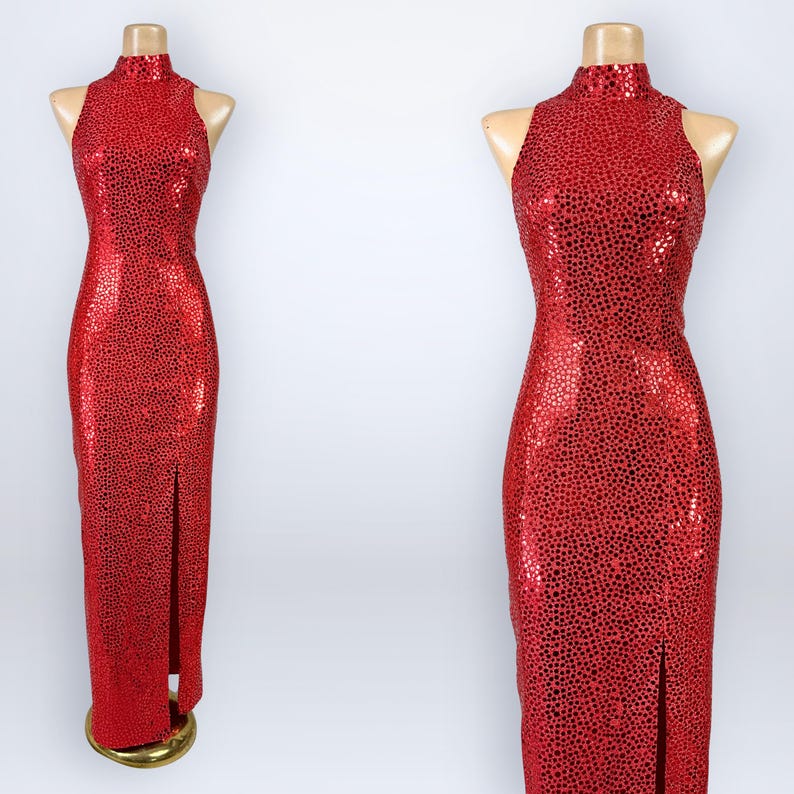 May include: A floor-length sleeveless dress in a vibrant red hue, featuring a high neckline and a dense, all-over pattern of small, reflective circular sequins. The garment includes a straight silhouette with a single side slit at the hem.