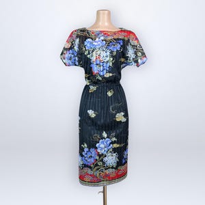 Puede incluir: Vestido negro con estampado floral con flores azules y blancas, detalles en rojo y cintura con banda. El vestido tiene mangas cortas y un dobladillo a la altura de la rodilla. El vestido se exhibe en un maniquí.