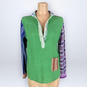 May include: A long-sleeve shirt featuring a solid green front panel with a three-button placket, a small brown striped pocket, and mismatched sleeves. The left sleeve is blue with a subtle pattern, while the right sleeve features a purple plaid design.