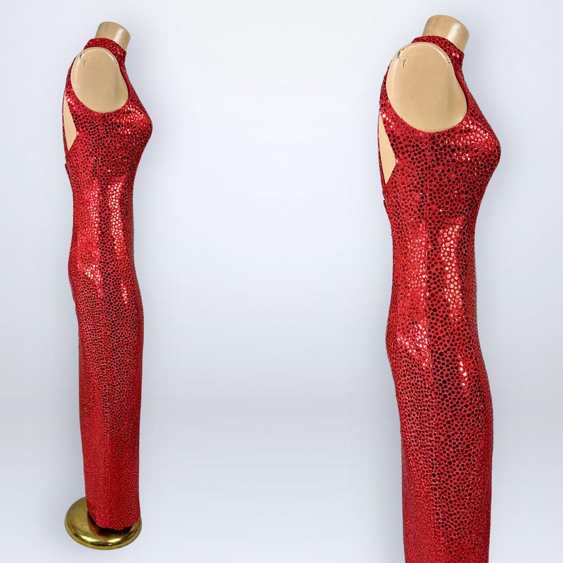 May include: A floor-length sleeveless dress in a vibrant red color, fully covered in small, reflective circular sequins. The garment features a high neckline, a fitted silhouette, and a cutout detail on the side of the bodice, displayed on a mannequin.