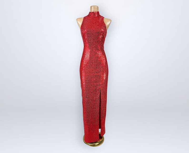 May include: A floor-length, sleeveless red dress featuring a high neckline and a dense pattern of small black spots. The garment is fitted through the torso and hips, extending to the floor with a straight hem and a single vertical slit on the front.