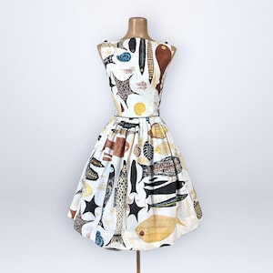 May include: A vintage-style dress on a mannequin, featuring a white background with a colorful fish pattern. The dress has a fitted bodice and a flared skirt, with a black trim at the waist. The fish illustrations are in shades of brown, black, yellow, and blue.