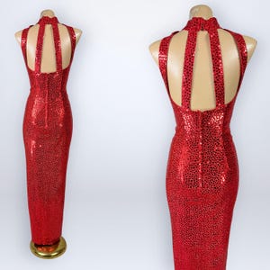 May include: A floor-length red dress featuring a shimmering, reflective dot pattern throughout. The garment has a high neckline, a racerback-style cutout design, and a vertical zipper closure running down the center of the back panel.