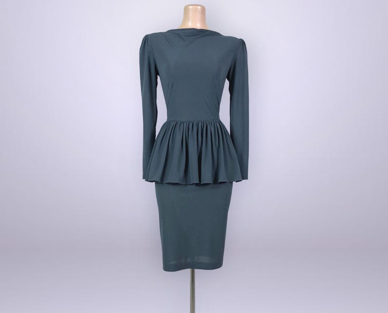 Puede incluir: Un vestido de color verde azulado con mangas largas y cintura peplum. El vestido tiene un corpi&ntilde;o ajustado y una falda l&aacute;piz hasta la rodilla. El vestido se exhibe en un maniqu&iacute; sobre un fondo liso. El vestido es de tela lisa.