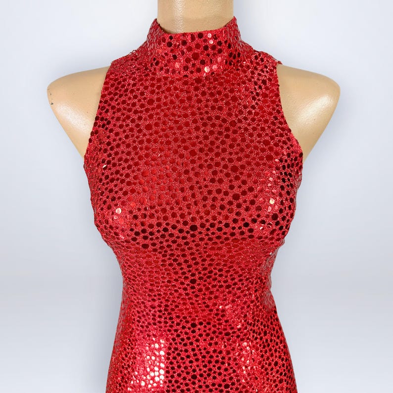 May include: A sleeveless red dress featuring a high mock neck collar and a dense, all-over sequin embellishment. The garment is fitted through the torso and displays a uniform, shimmering texture created by the small, circular red sequins.