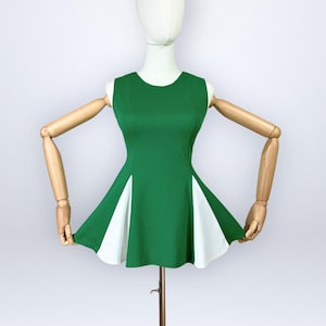 Könnte beinhalten: Ein ärmelloses Kleid mit einem einfarbig grünen Oberteil und einem ausgestellten Rock mit abwechselnden weißen dreieckigen Einsätzen. Das Kleidungsstück wird auf einer Schaufensterpuppe mit beweglichen Holzarmen präsentiert.