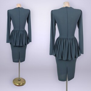 Puede incluir: Un vestido de color verde azulado con mangas largas y cintura peplum. El vestido tiene una falda l&aacute;piz ajustada y una abertura en la espalda. El vestido se exhibe en un maniqu&iacute;.