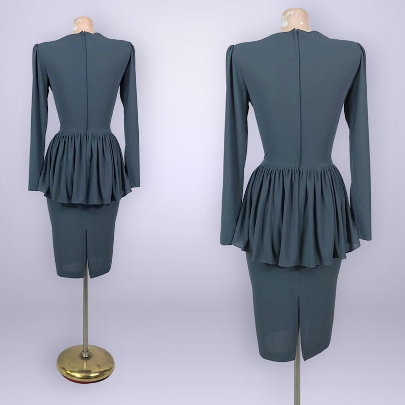 Puede incluir: Un vestido de color verde azulado con mangas largas y cintura peplum. El vestido tiene una falda l&aacute;piz ajustada y una abertura en la espalda. El vestido se exhibe en un maniqu&iacute;.