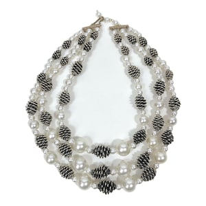 Puede incluir: Collar de tres hilos con perlas de imitación blancas y detalles metálicos en negro y plateado. El collar tiene un diseño clásico con un cierre seguro. Adecuado para ocasiones formales.