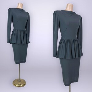 Puede incluir: Un vestido de color verde azulado con mangas largas y cintura peplum. El vestido tiene una falda l&aacute;piz ajustada y un cuello alto. El vestido se exhibe en un maniqu&iacute;. El vestido es de estilo vintage.