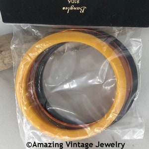 May include: A set of three circular bangles in yellow, brown, and black, enclosed in a clear plastic bag. The black header card features the text 8106 and Bangles in gold lettering. The bottom of the image displays the text Amazing Vintage Jewelry.