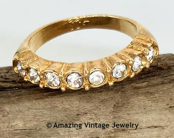 May include: A gold-toned ring featuring a row of seven clear, round-cut stones set into a textured metal band. The interior of the band is engraved with text. The image includes the text Amazing Vintage Jewelry at the bottom.