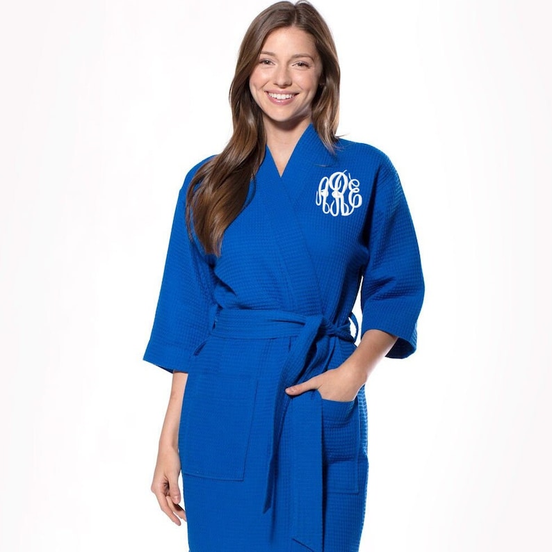 May include: A royal blue waffle weave robe with a white monogram on the left chest. The robe has a self-tie belt and two patch pockets.