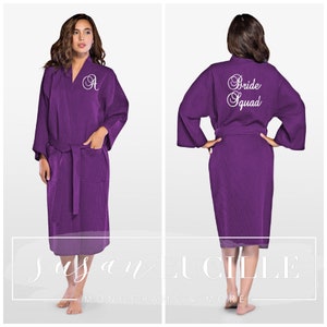 May include: Purple waffle weave robe with a white embroidered initial "A" on the left side and "Bride Squad" on the back.