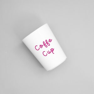 May include: A white coffee cup with the words "Coffee Cup" in pink script. The cup is cylindrical and angled slightly to the left against a grey background. The text is in a handwritten style.