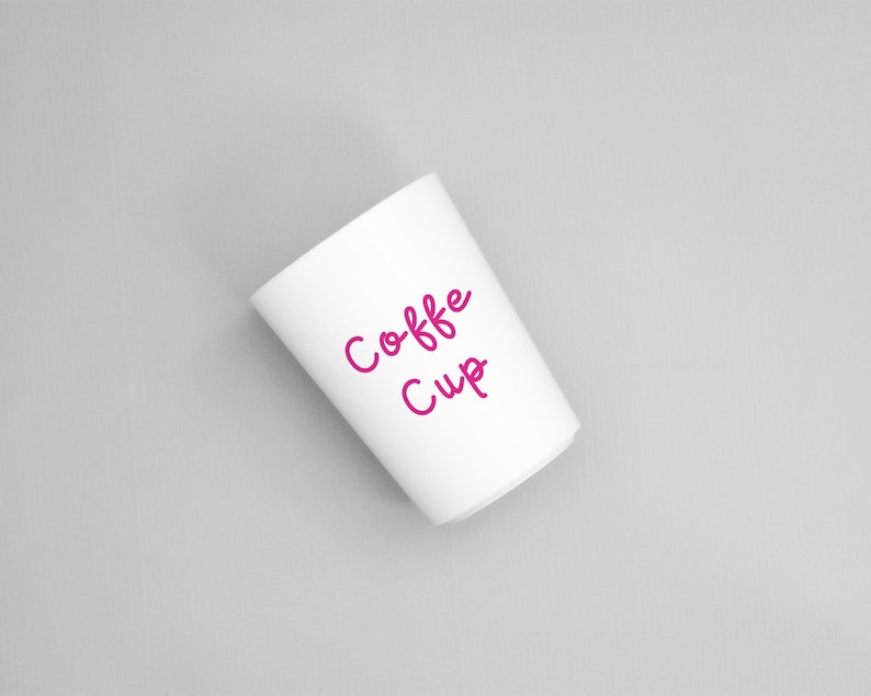 May include: A white coffee cup with the words "Coffee Cup" in pink script. The cup is cylindrical and angled slightly to the left against a grey background. The text is in a handwritten style.