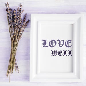 K&ouml;nnte beinhalten: Ein wei&szlig; gerahmter Druck mit den Worten "LOVE WELL" in dunkelblauer gotischer Schrift. Links vom Rahmen befindet sich ein B&uuml;ndel getrockneten Lavendels, vor einem hellvioletten Holzgrund.