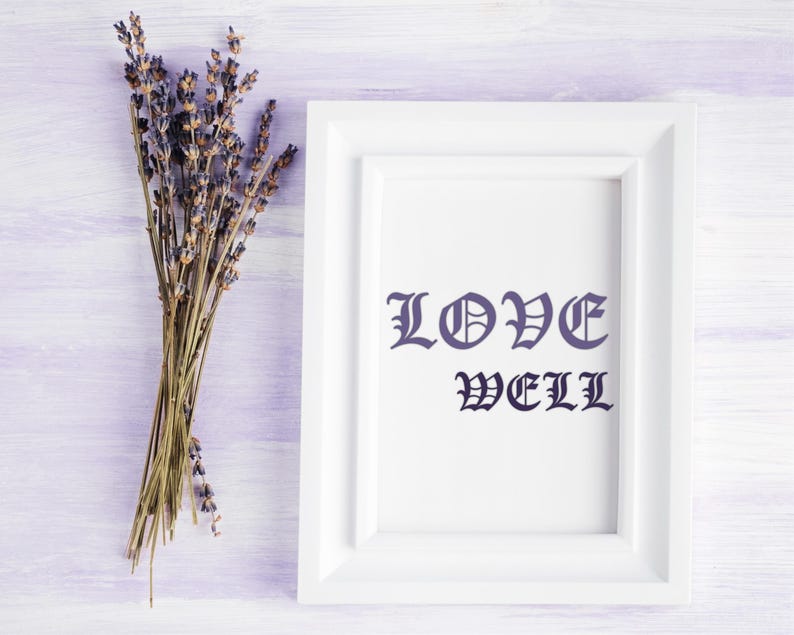 K&ouml;nnte beinhalten: Ein wei&szlig; gerahmter Druck mit den Worten "LOVE WELL" in dunkelblauer gotischer Schrift. Links vom Rahmen befindet sich ein B&uuml;ndel getrockneten Lavendels, vor einem hellvioletten Holzgrund.