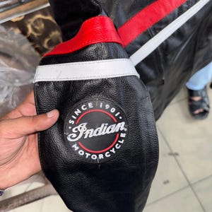 May include: Black leather motorcycle jacket with red and white accents. Features a circular patch with "Indian Motorcycle" text and the words "Since 1901". The jacket has a classic design with a focus on durability and style.