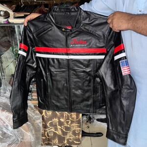 May include: Black leather motorcycle jacket with red and white stripes across the chest and sleeves. The jacket features the text "Indian Motorcycle" in red script and an American flag patch on the sleeve.